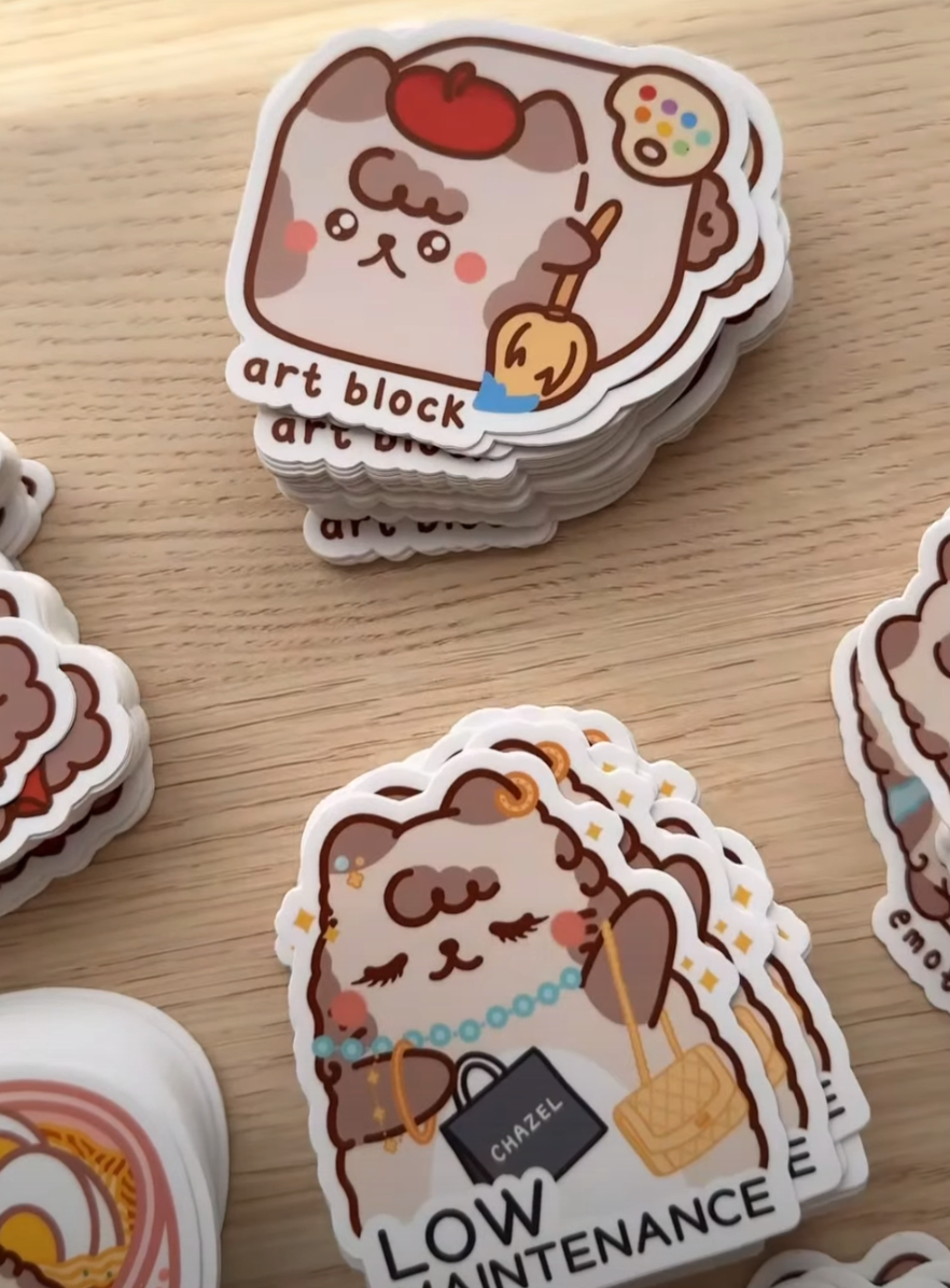 Milkteanco2.png Milkteanco cozy pastel die-cut stickers featuring a cute bear-character 'art block' design and a 'LOW MAINTENANCE' shopping bear sticker stack on a wooden surface
