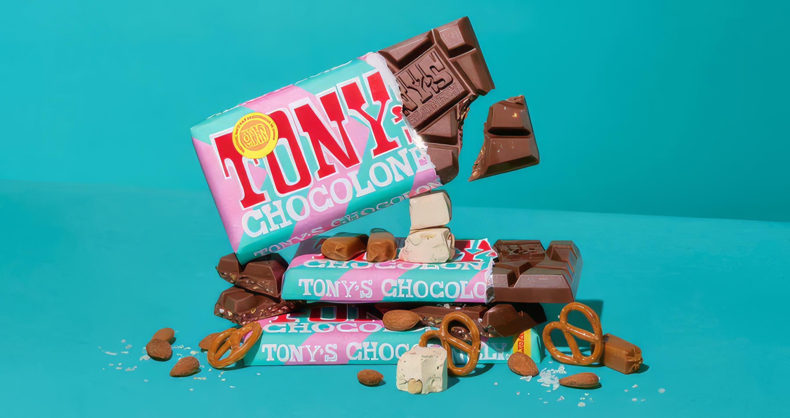 Stack of Tony's Chocolonely bars on a teal background with broken chocolate, almonds, pretzels, and nougat pieces spilling around them
