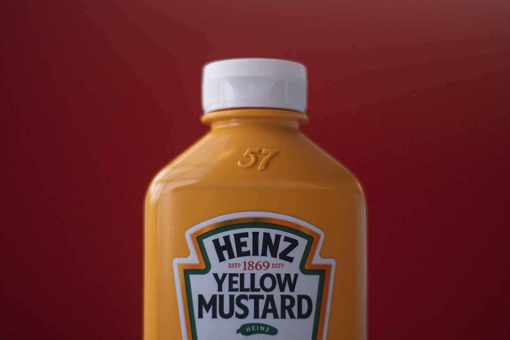 Heinz Yellow Mustard bottle on a deep red background with the brand's keystone-shaped label