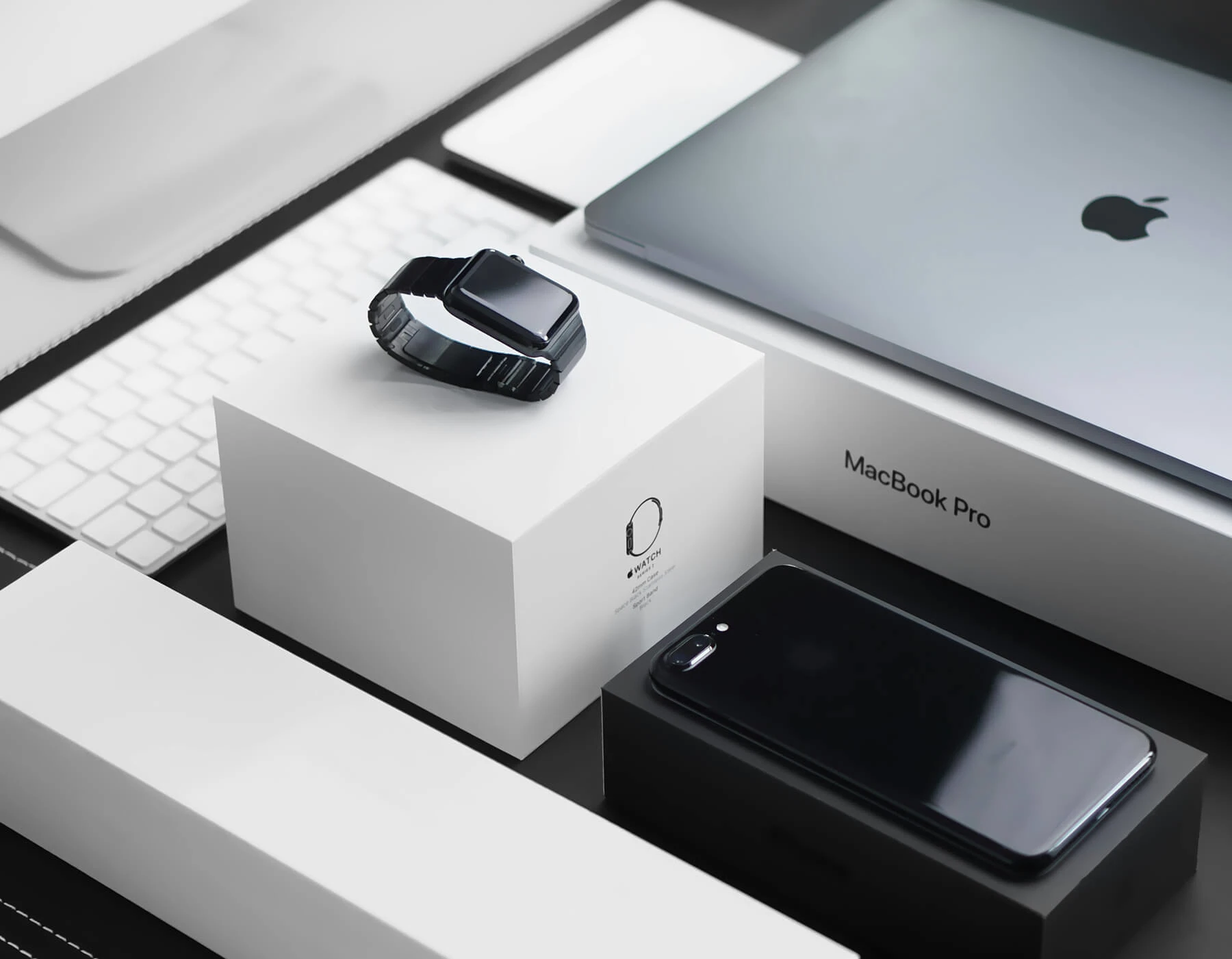 Apple Watch, MacBook Pro, and iPhone arranged on monochrome packaging with minimal product details