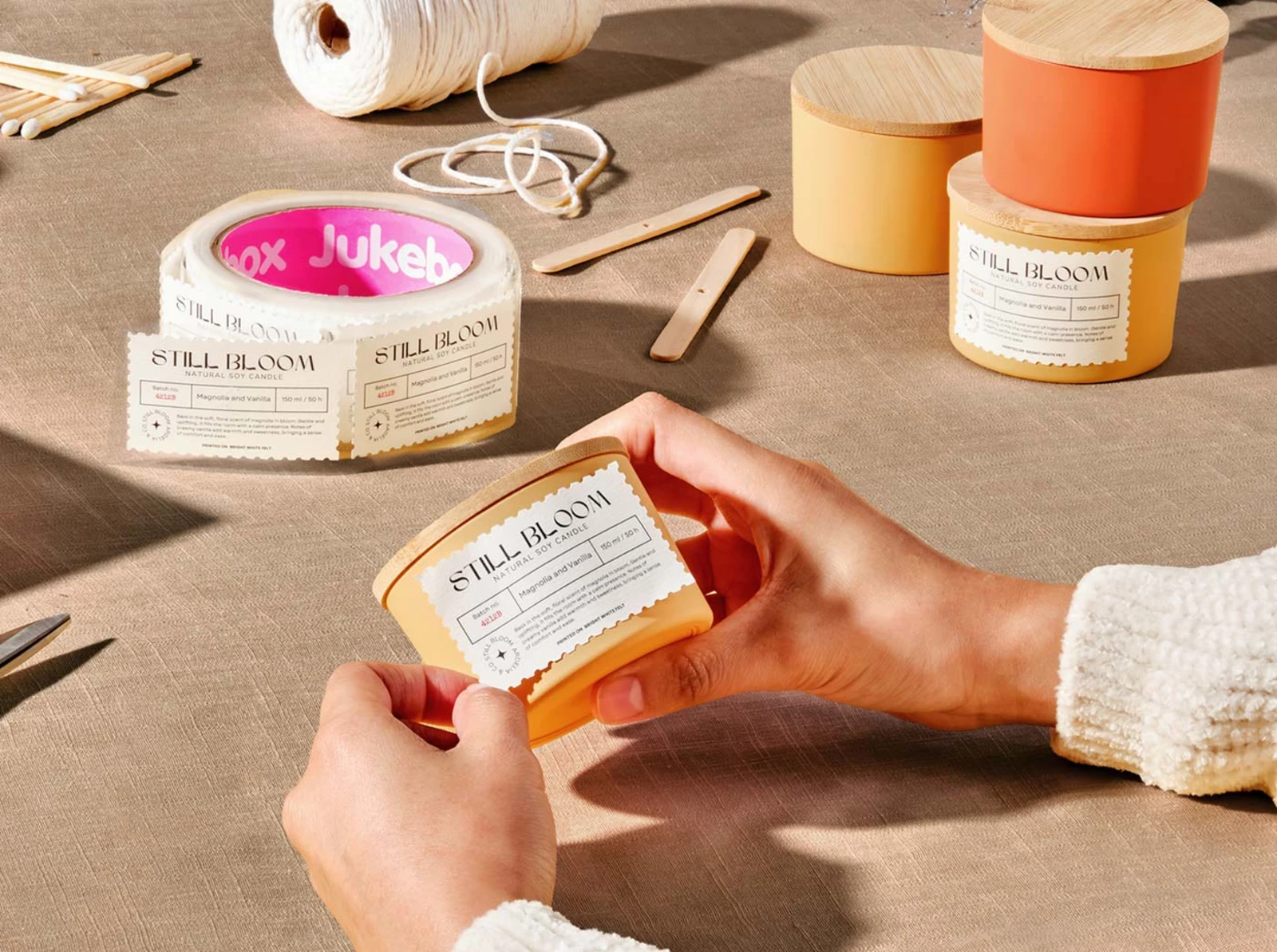 Someone attaching a white premium roll label to an orange candle jar.
