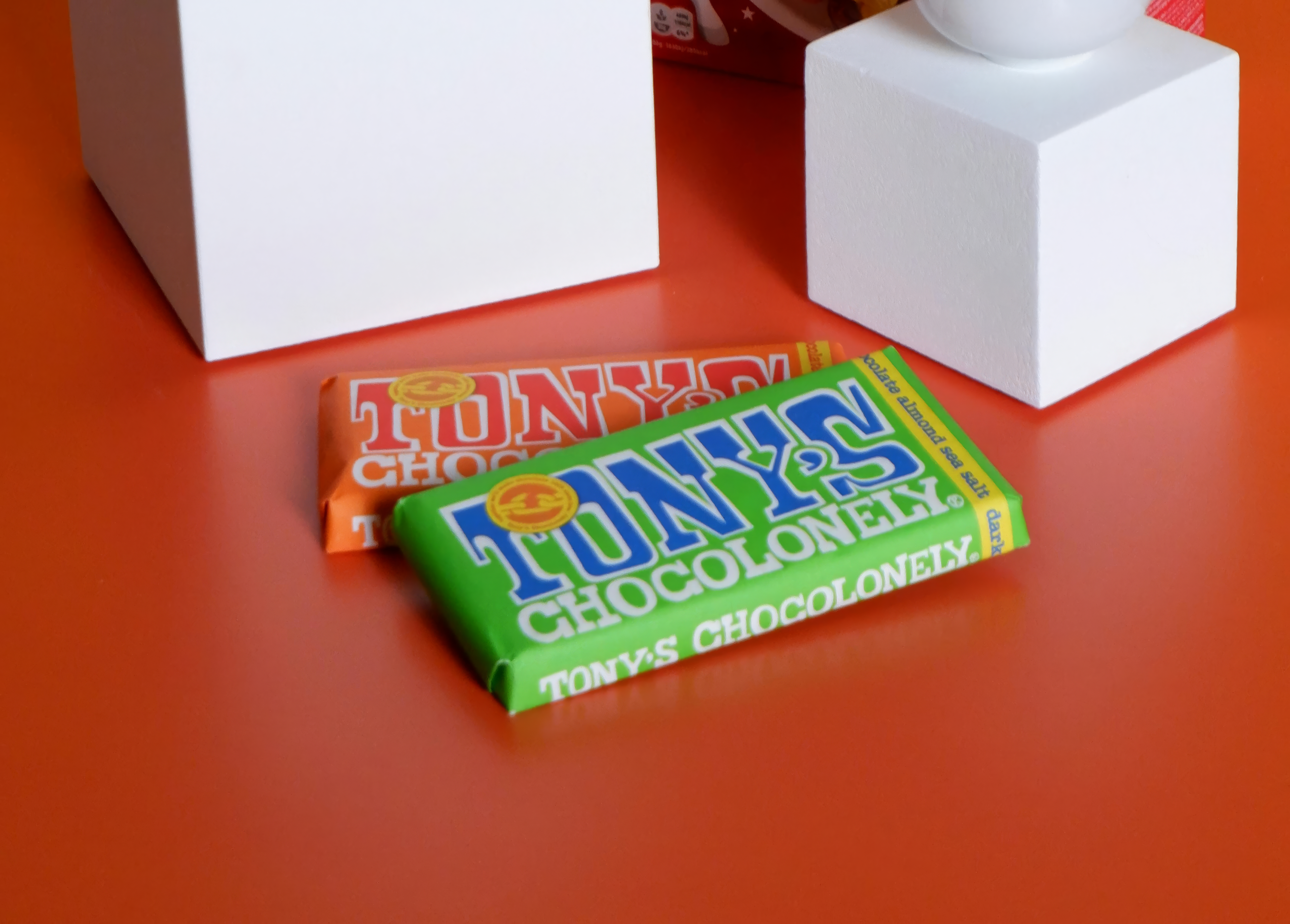 pexels-iremmeric-12541477 (1)-upscaled-2x.png Tony's Chocolonely chocolate bar on a bright orange background styled with Kellogg's Froot Loops and cereal bowls